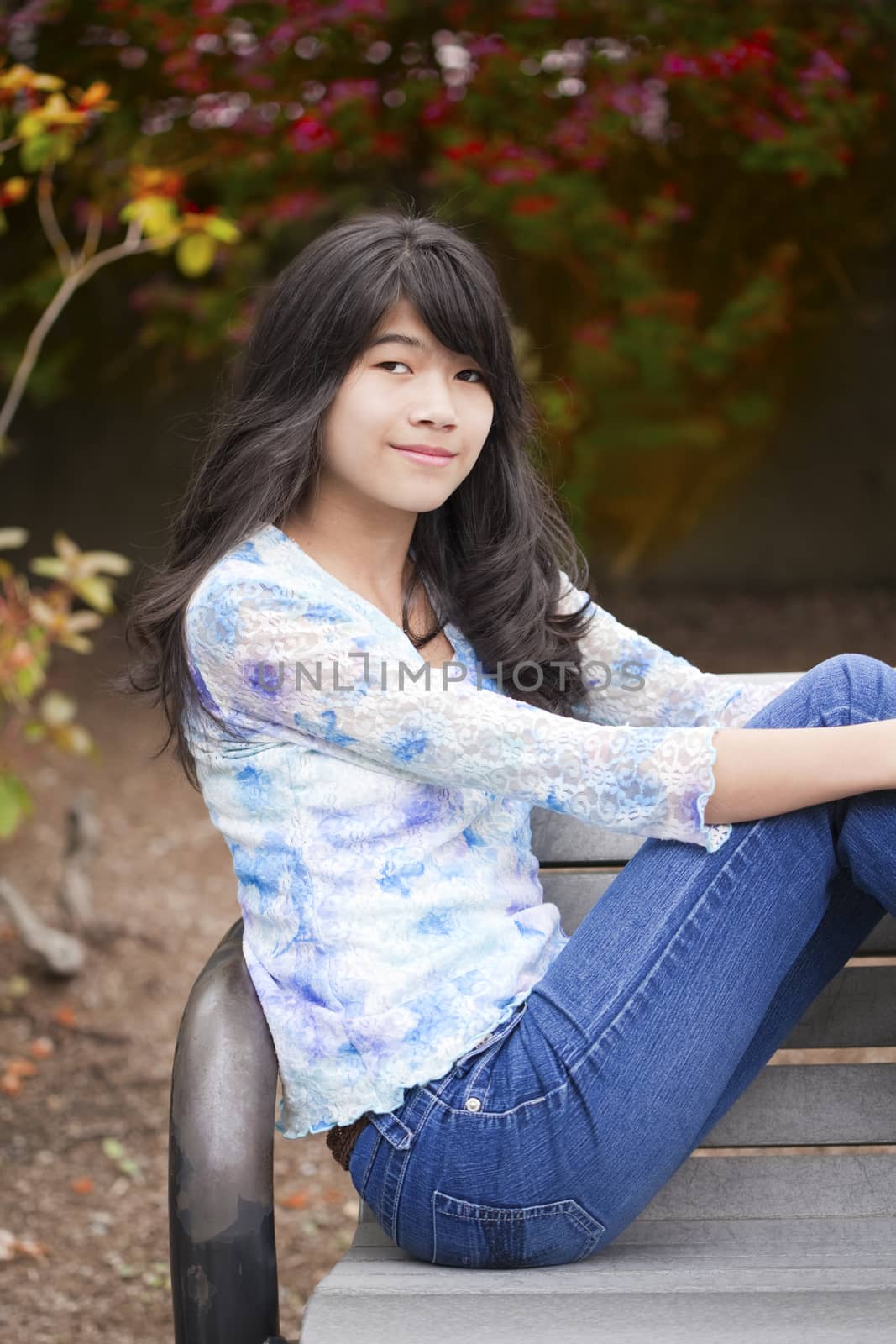 Young biracial preteen girl ejoying outdoors, sitting on wooden park bench