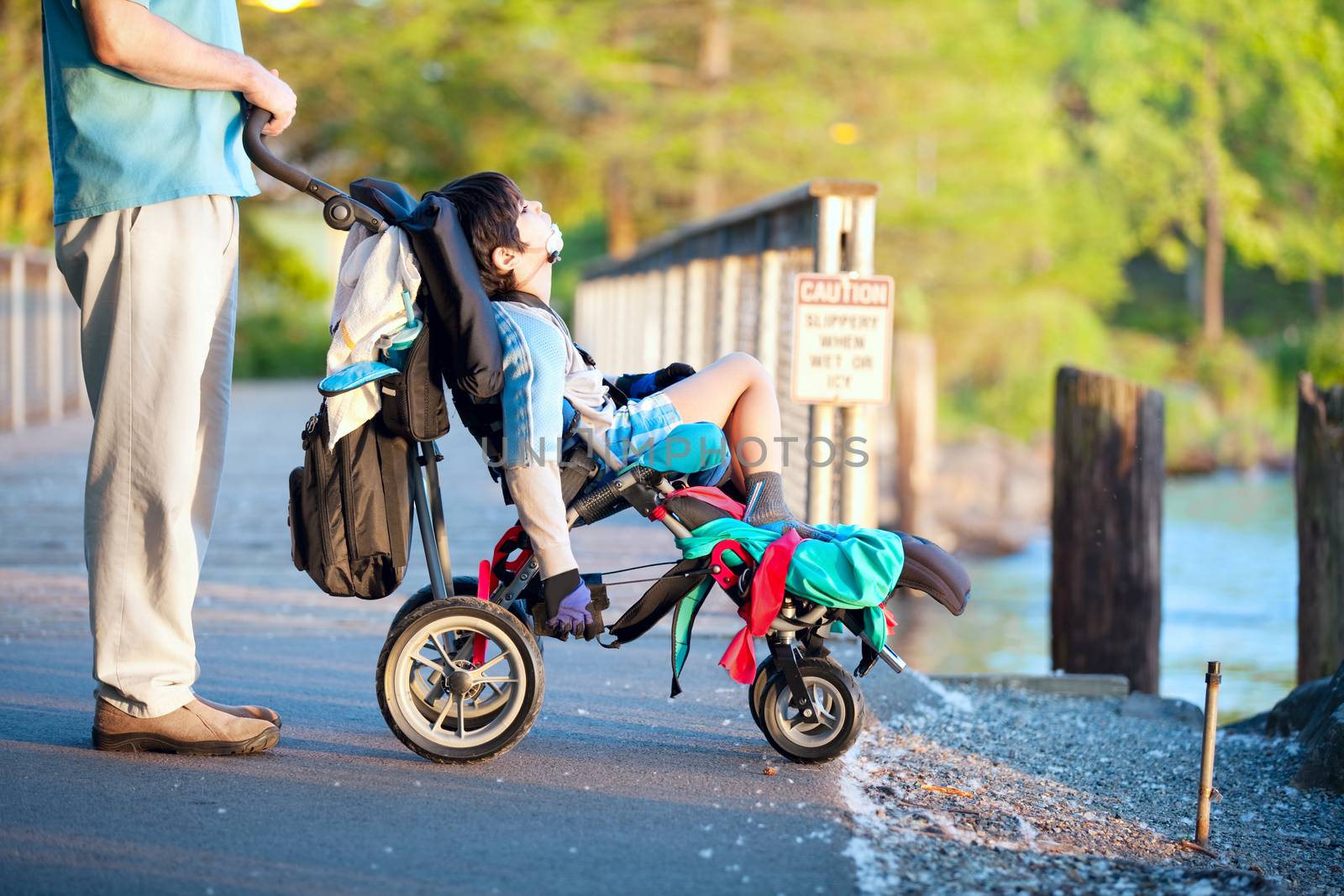 Father with disabled son in wheelchair outdoors  at park, enjoying sunset