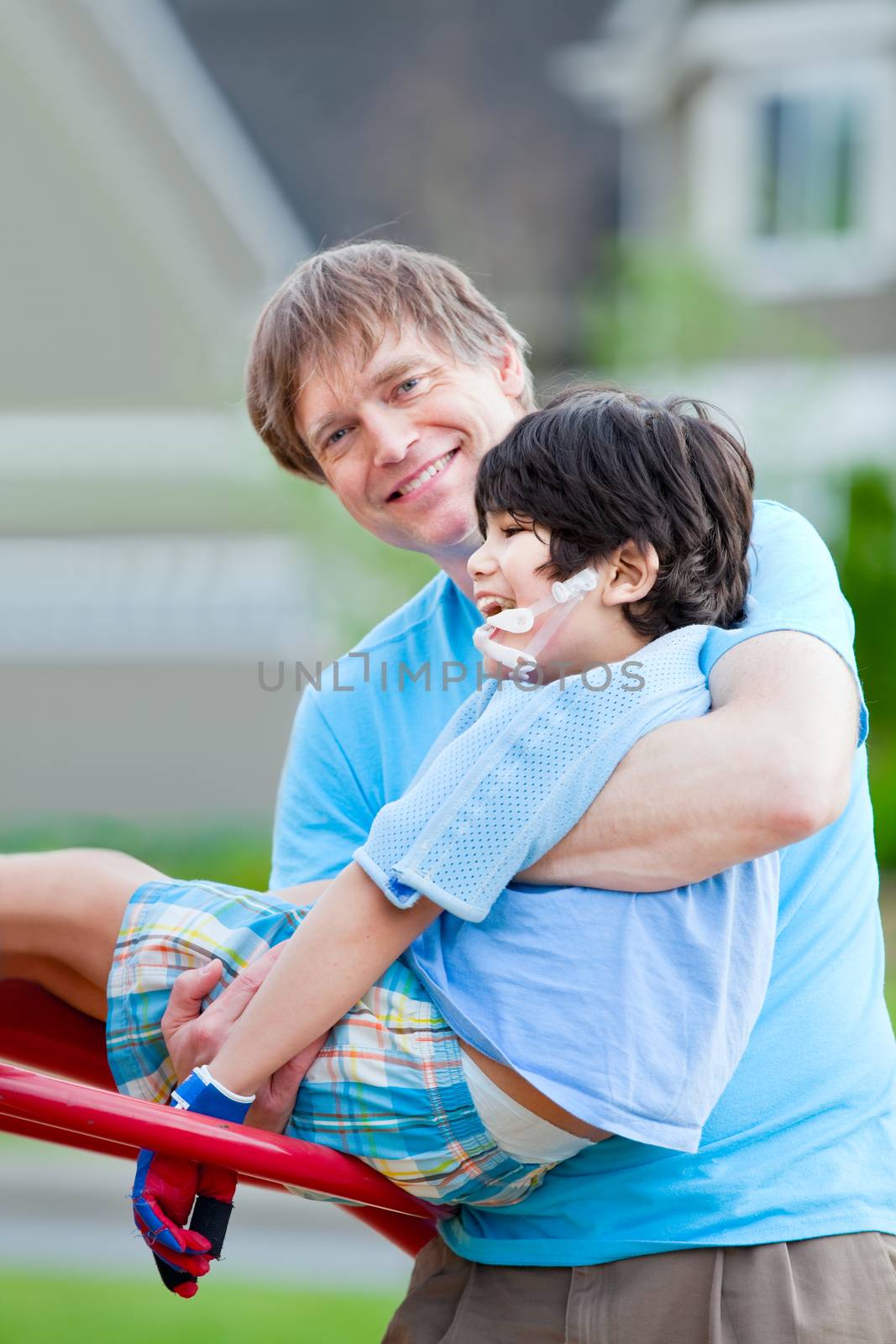 Father helping disabled seven year old son play on playground equipment