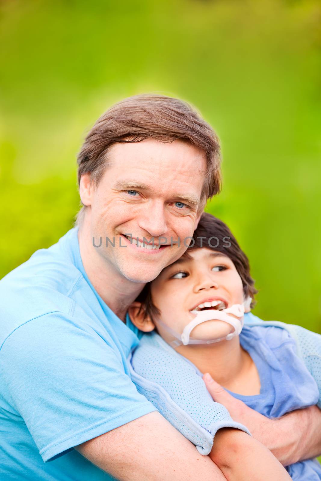 Handsome father sitting with smiling disabled seven year old son outdoors