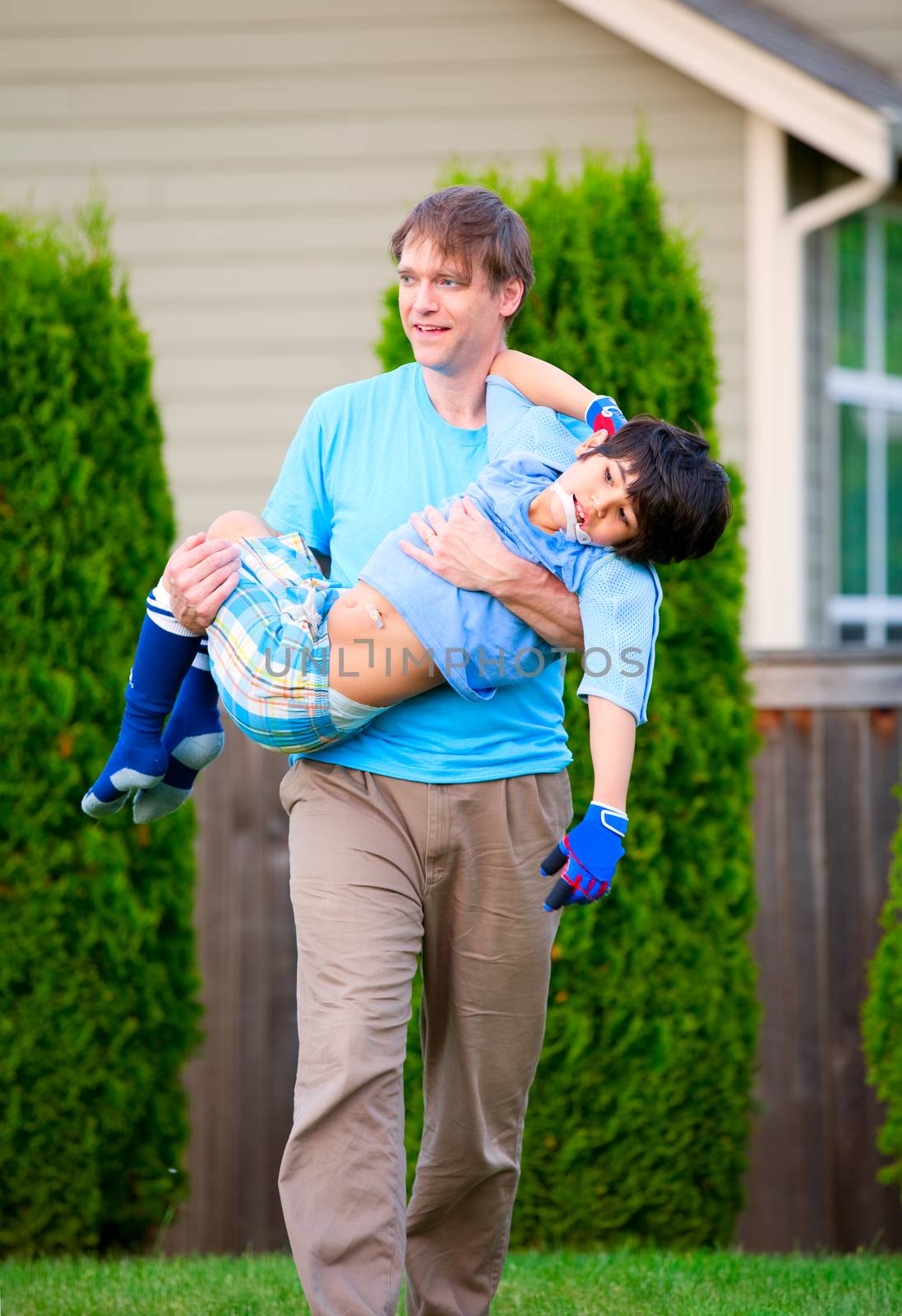 Father carrying disabled seven year son outdoors