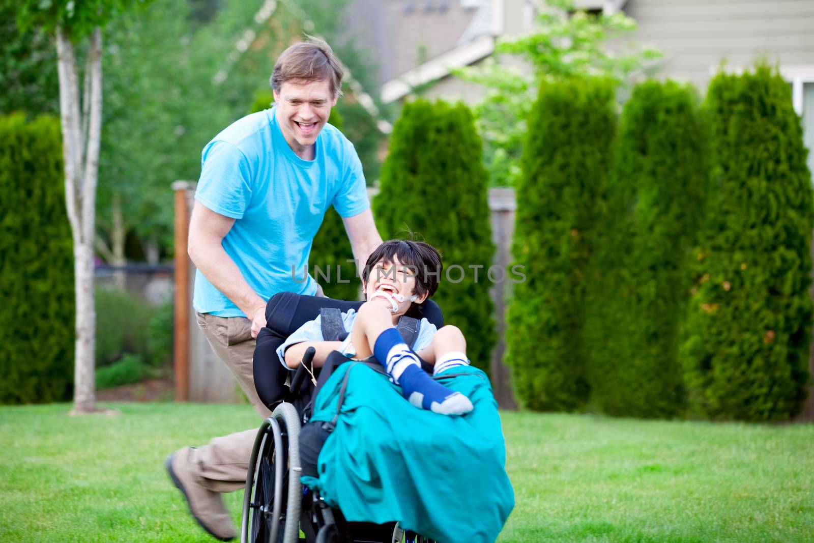 Father racing around park with disabled son in wheelchair by jarenwicklund