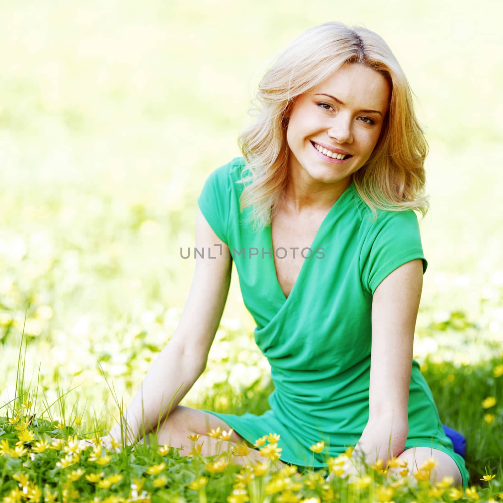 Beautiful young blond woman sitting on grass in park and enjoyng flowers