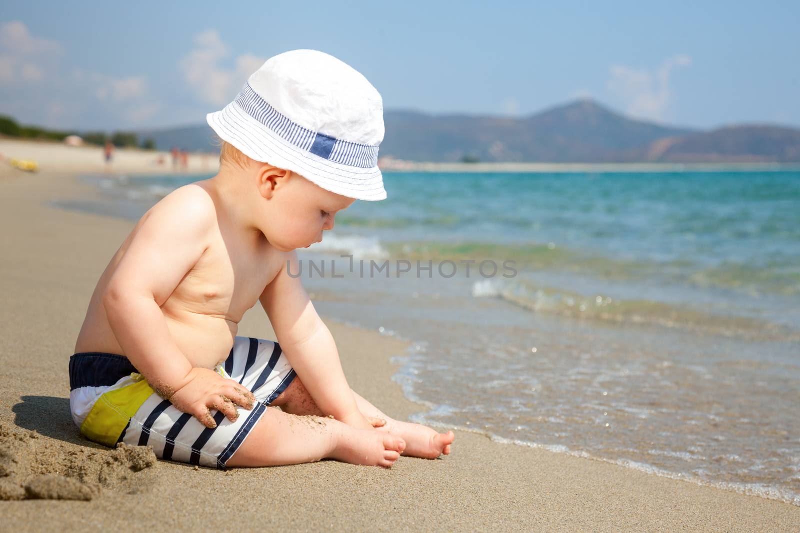 Baby boy wearing hat and shorts playing on a beach