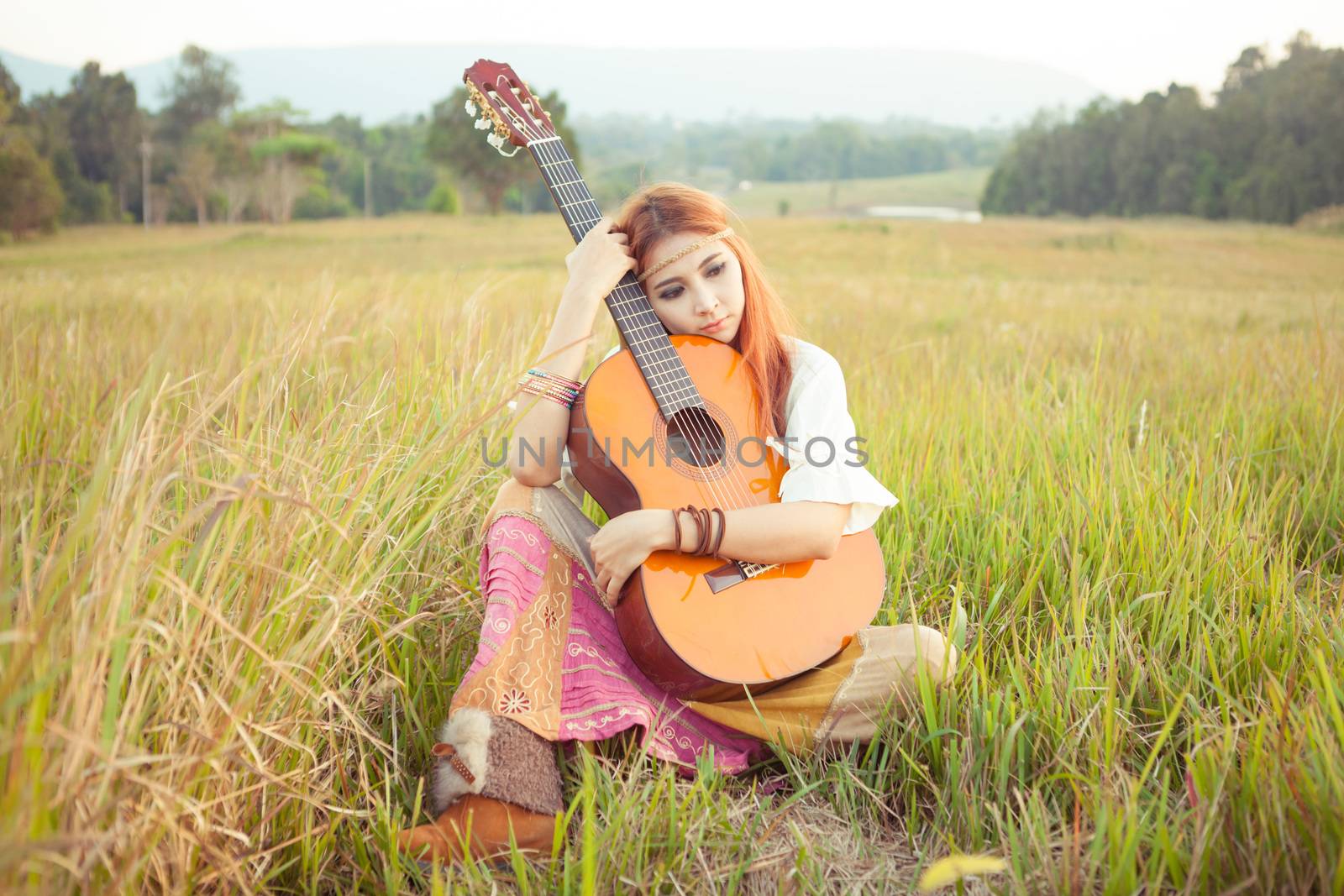 Pretty country hippie girl playing guitar on grass