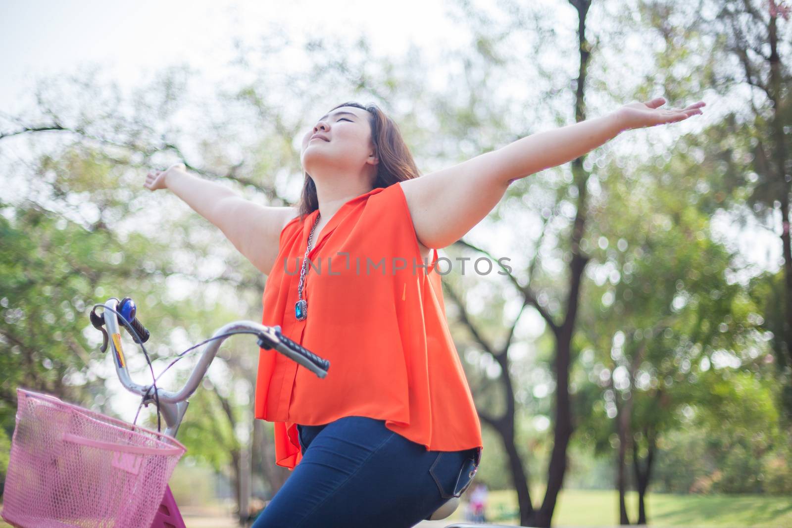 Happy fatty asian woman outstretched with bicycle outdoor in a park