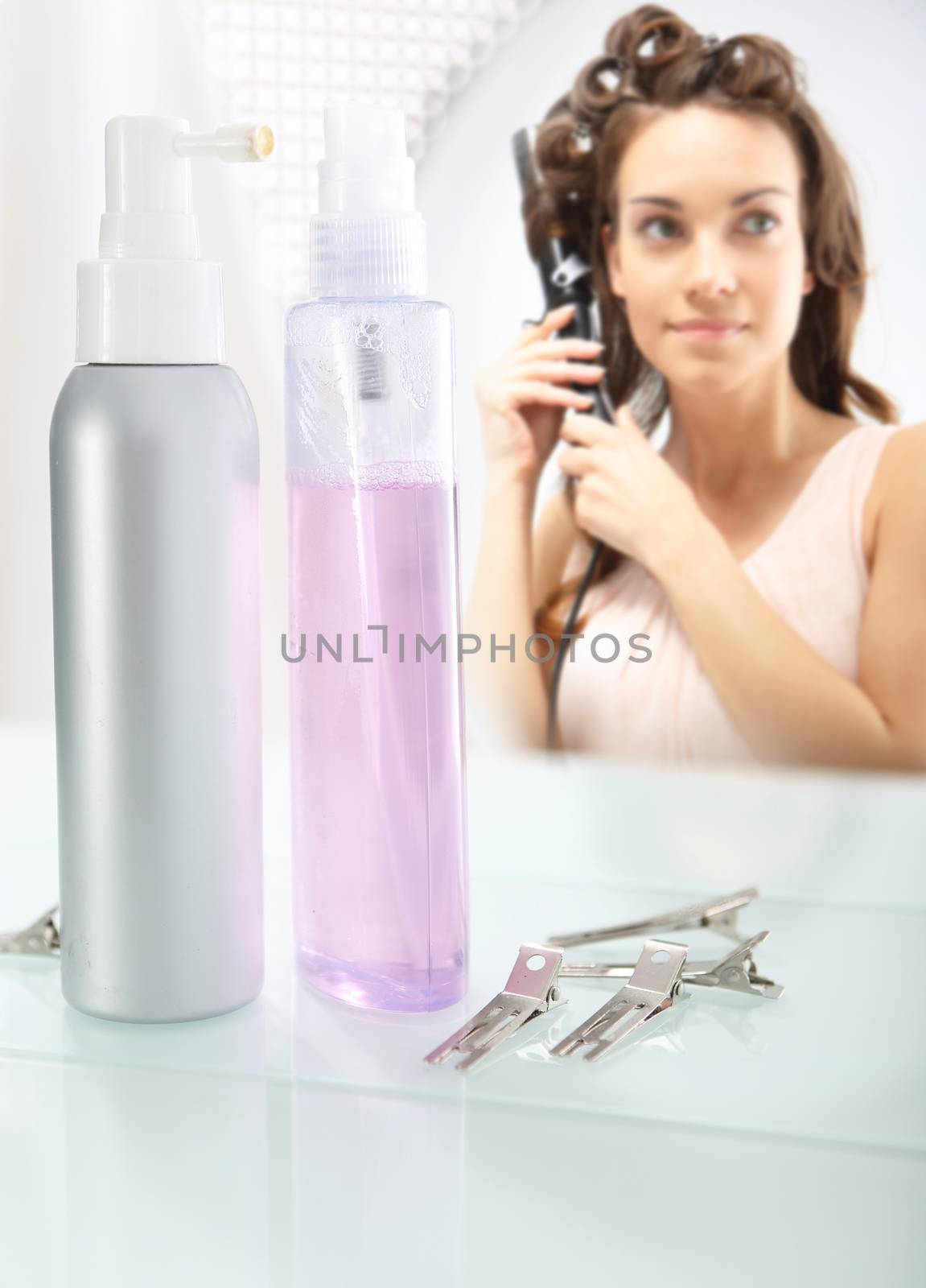 Young girl winds up hair curling iron standing in front of the bathroom mirror. by robert_przybysz