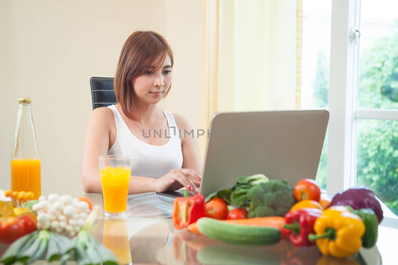Young asian woman drinking orange juice and using internet at home