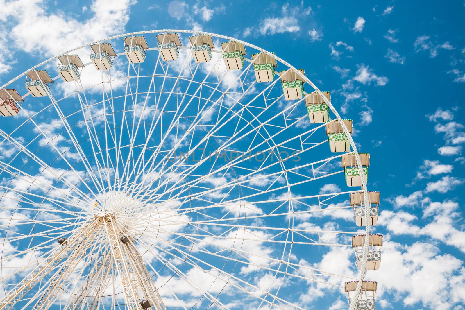 Ferris wheel of fair and amusement park.  White clouds in the blue sky in background.