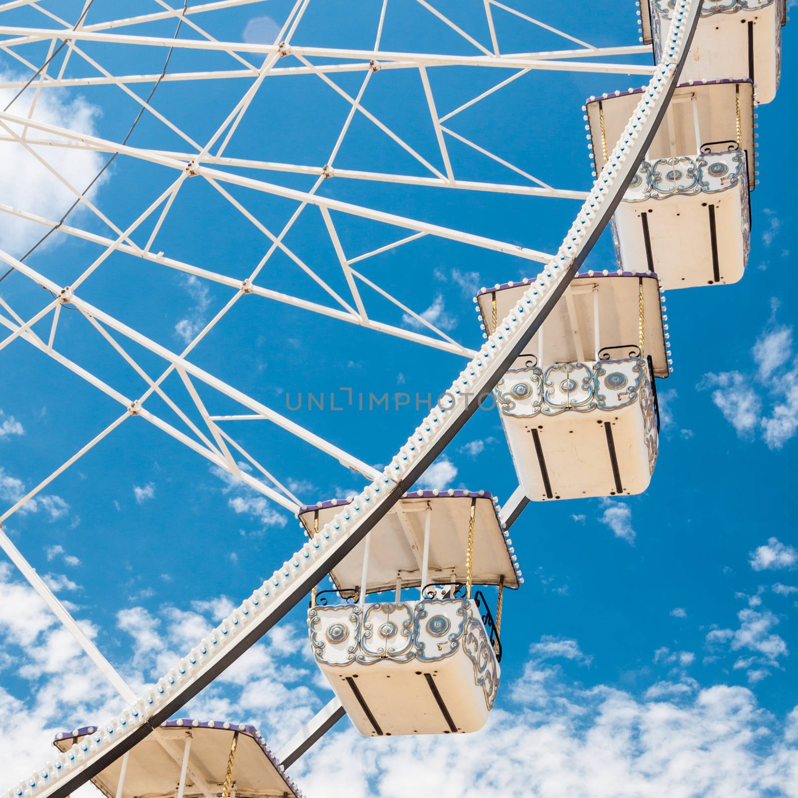 Ferris wheel of fair and amusement park.  White clouds in the blue sky in background.