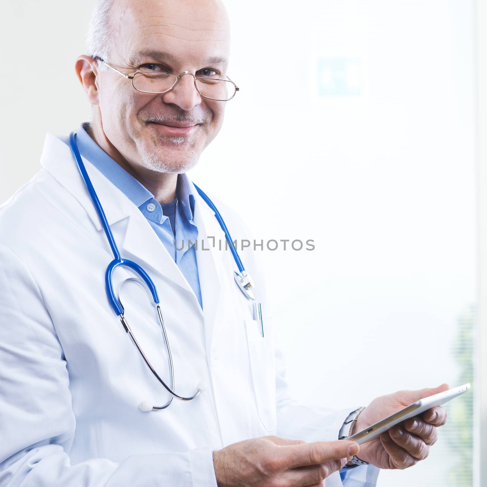 Senior friendly doctor using a tablet and smiling.