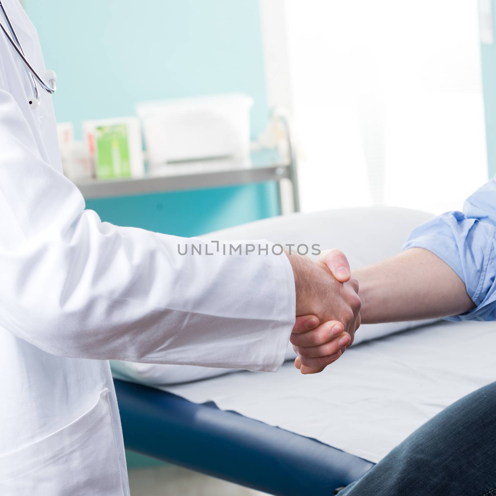 Doctor and patient handshake with medical equipment on the background.
