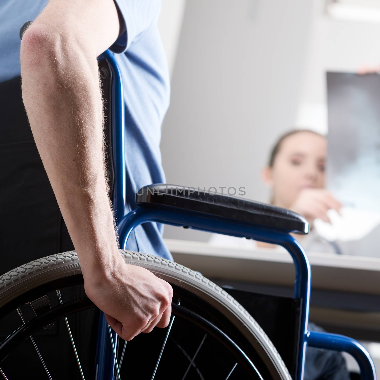 Disabled young man in wheelchair at doctors office. Doctor is looking x-ray 