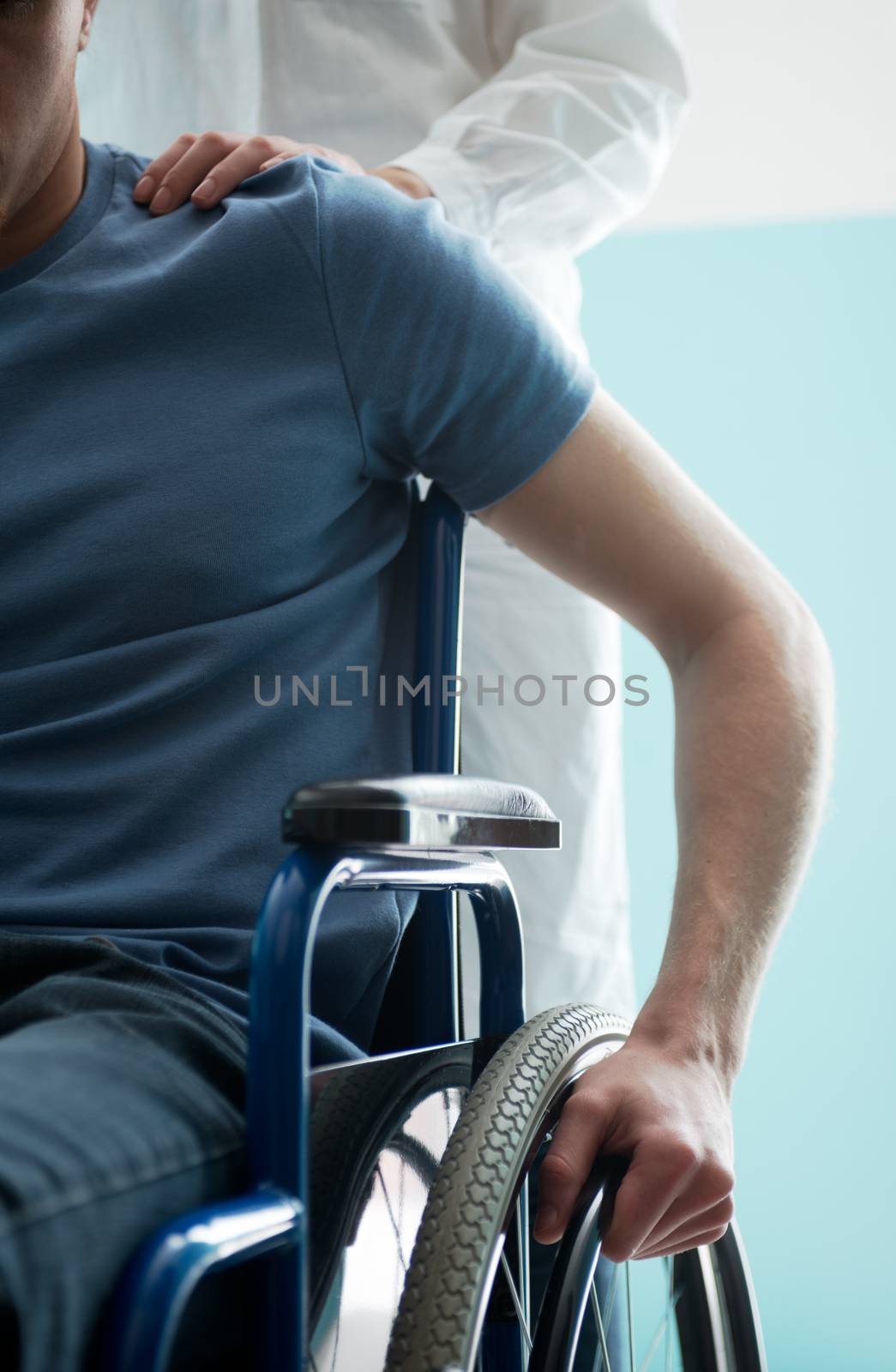 Doctor consoling young man sitting in wheelchair by stokkete