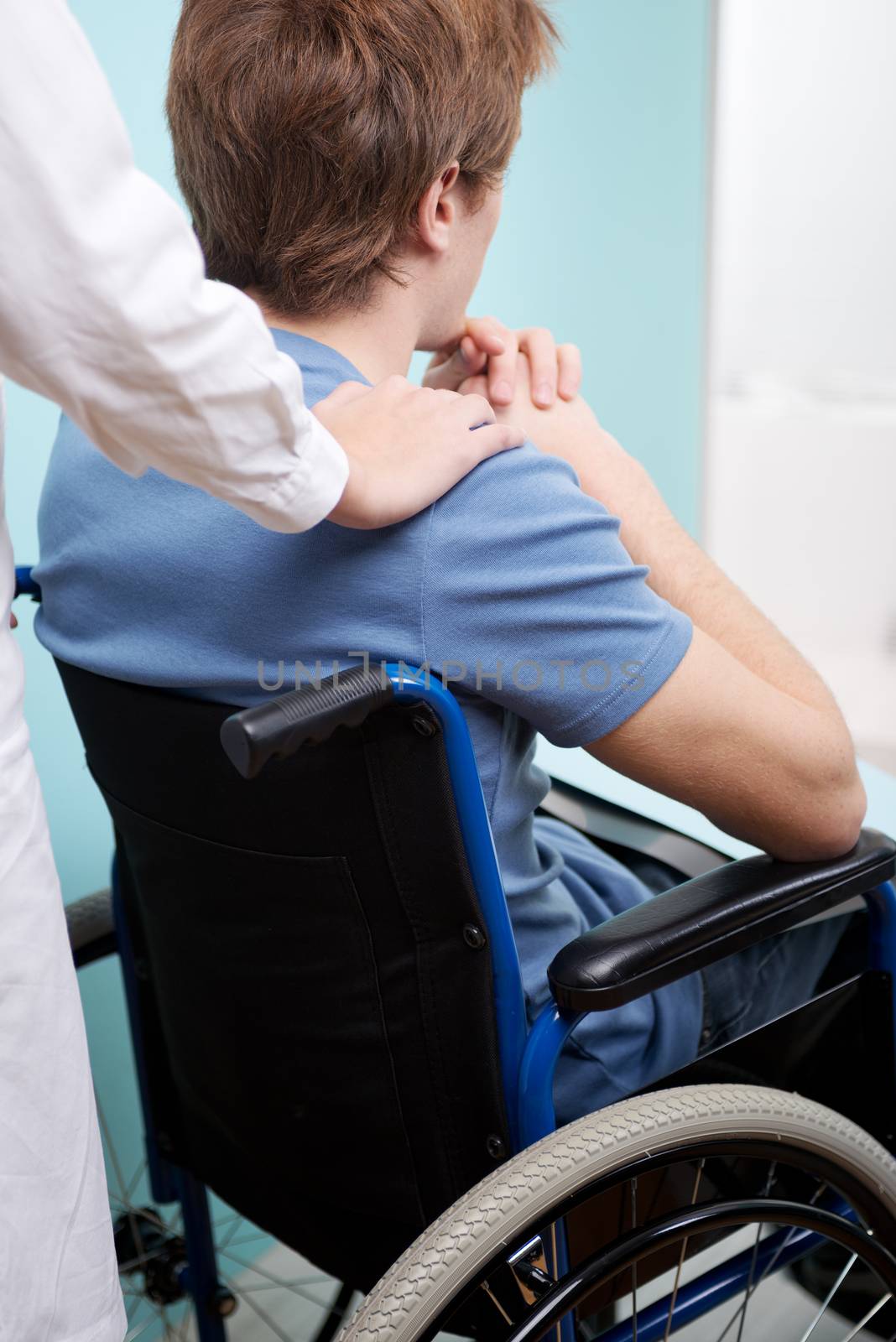 Doctor consoling young man sitting in wheelchair by stokkete