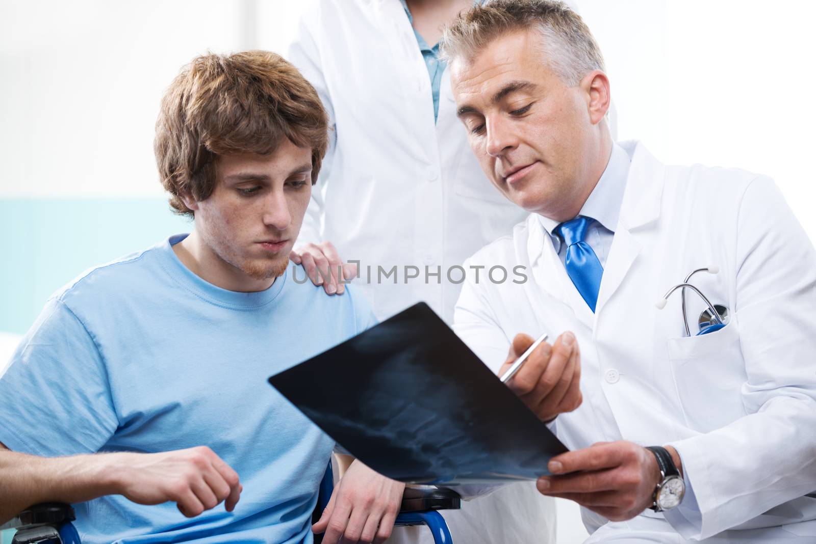 Doctor and assistant examining an x-ray image with a patient in wheelchair.