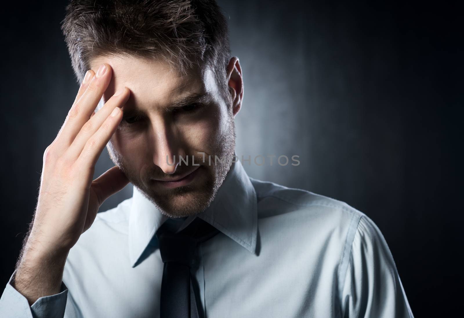 Exhausted young businessman with headache touching his head.