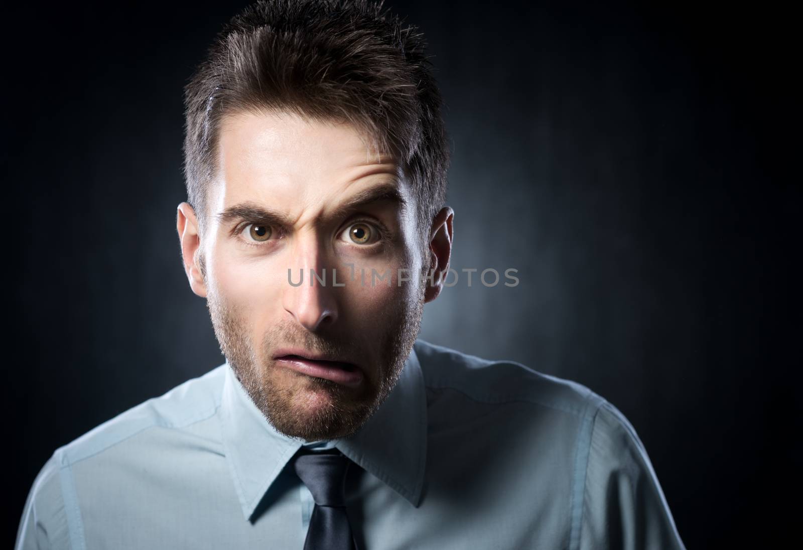 Distraught young businessman with raised eyebrow on gray background.