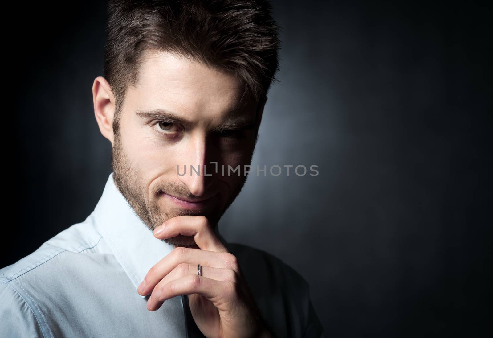 Young confident businessman looking at camera and touching his chin.