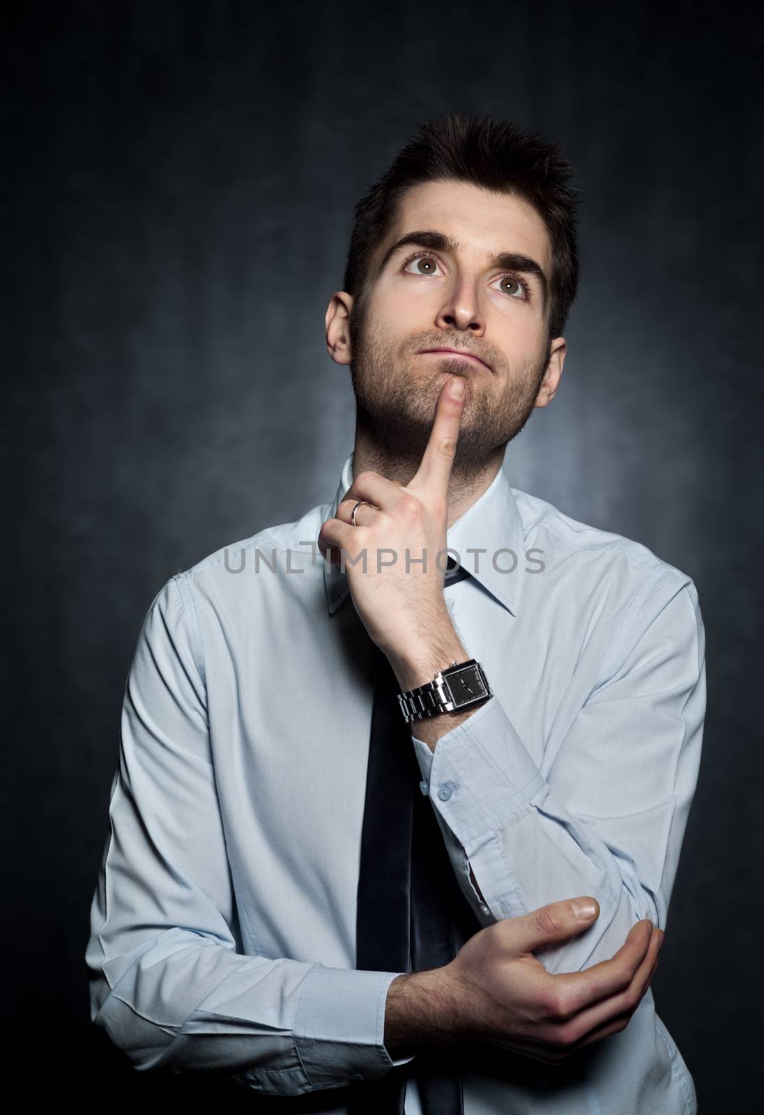 Young man thinking with finger on his chin on dark background.