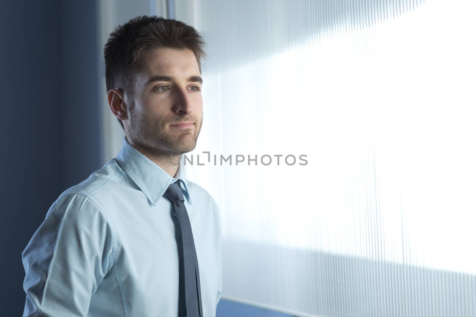 Young businessman at window looking away and thinking.