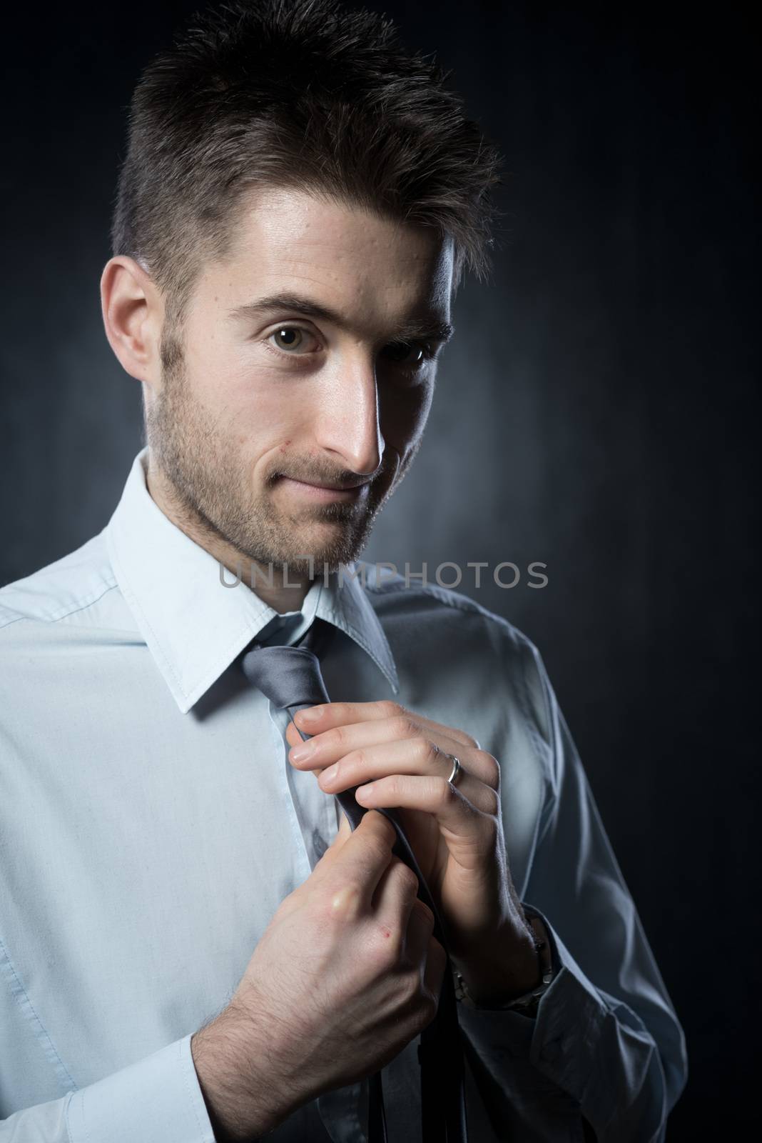 Young elegant man adjusting tie knot and smiling.