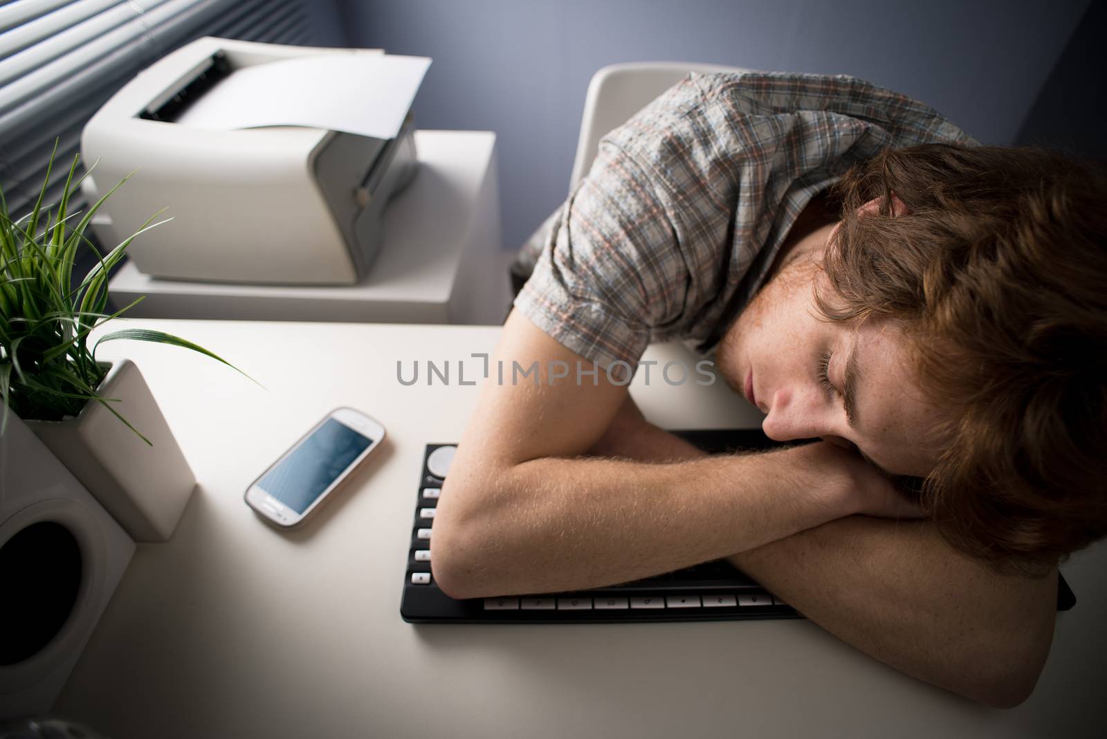 Young tired man sleeping on keyboard at office.