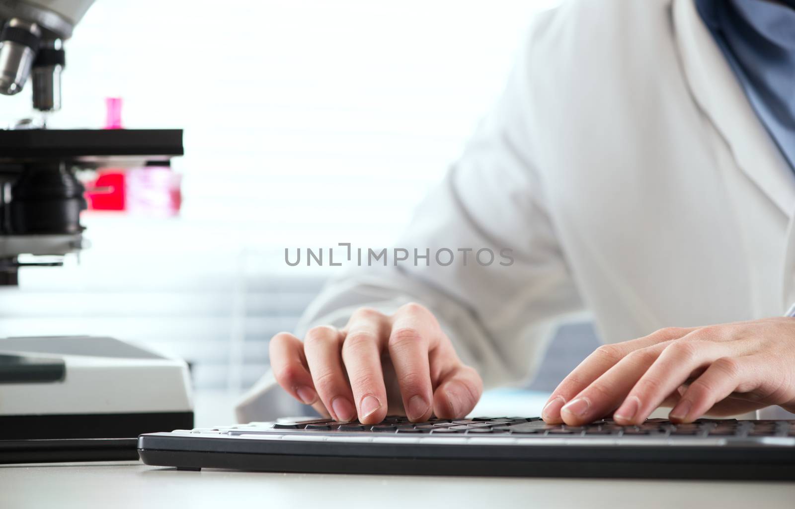 Researcher working at desk and typing on a keyboard with microscope and laboratory glassware.