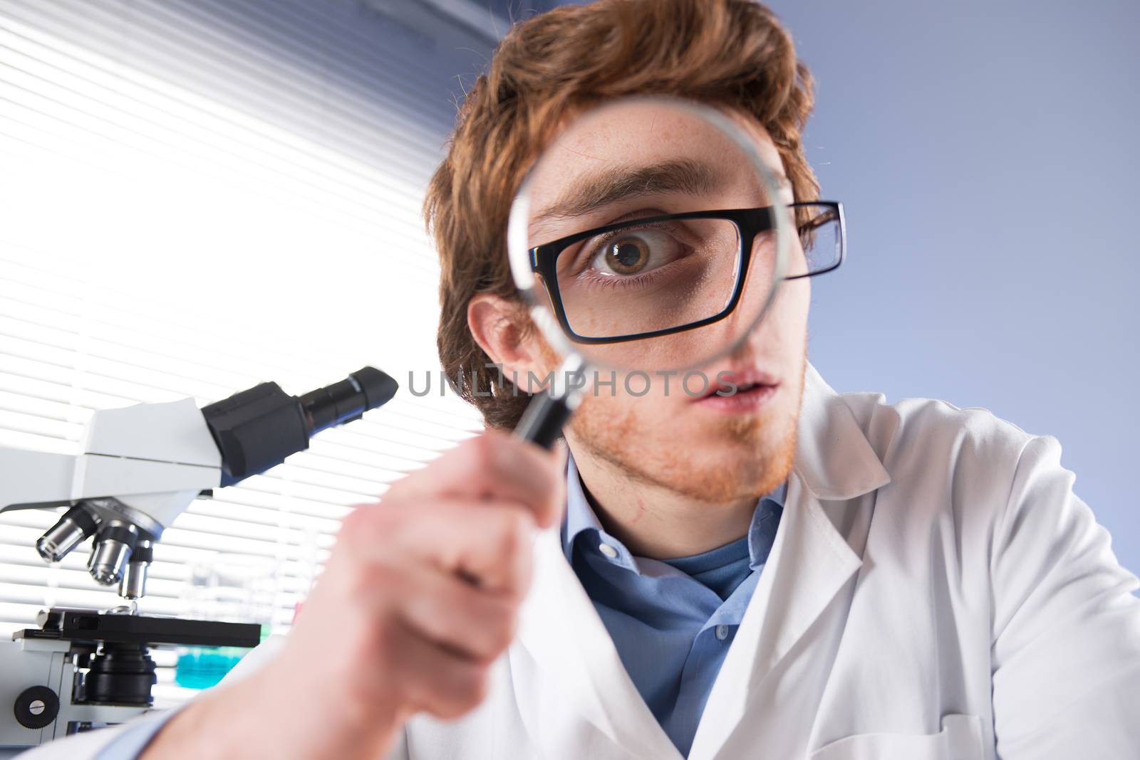 Young researcher looking through magnifier with surprised expression.