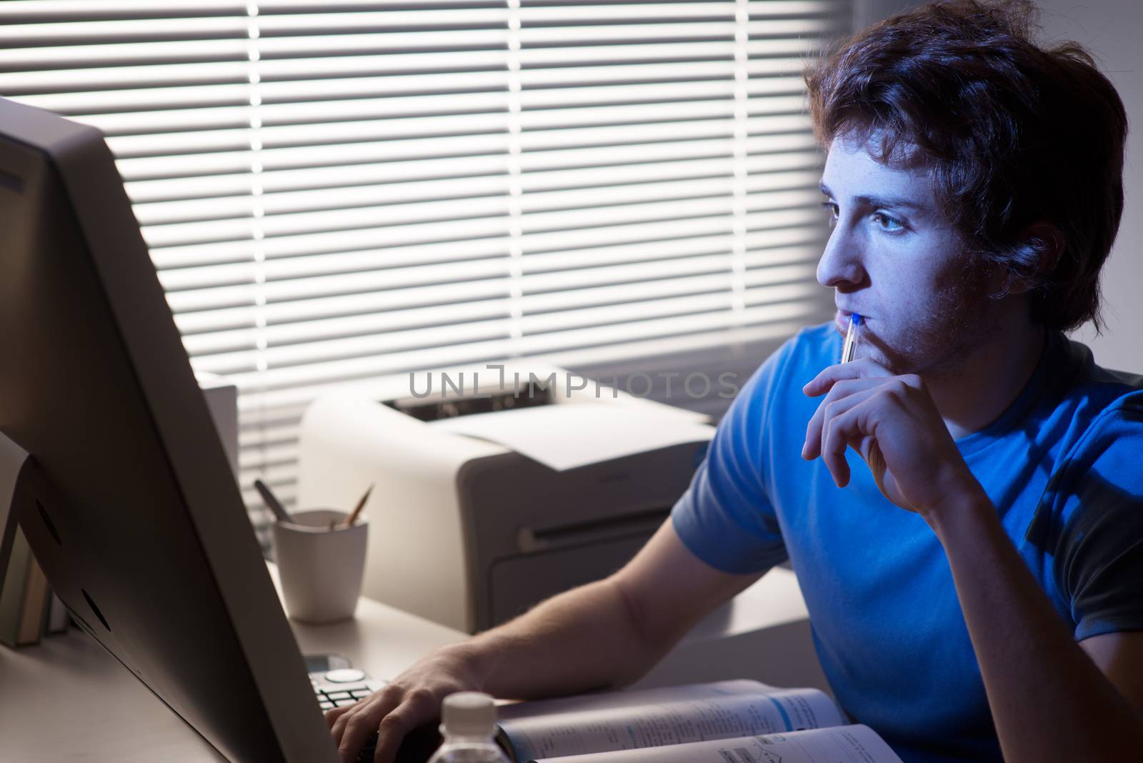 Young man staring at computer and holding a pen with office on background.