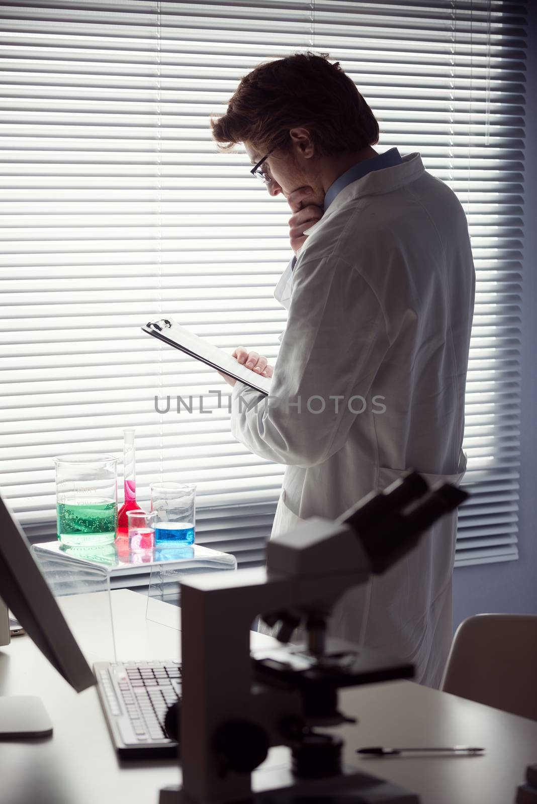 Researcher reading medical records in the chemical laboratory with microscope on foreground.