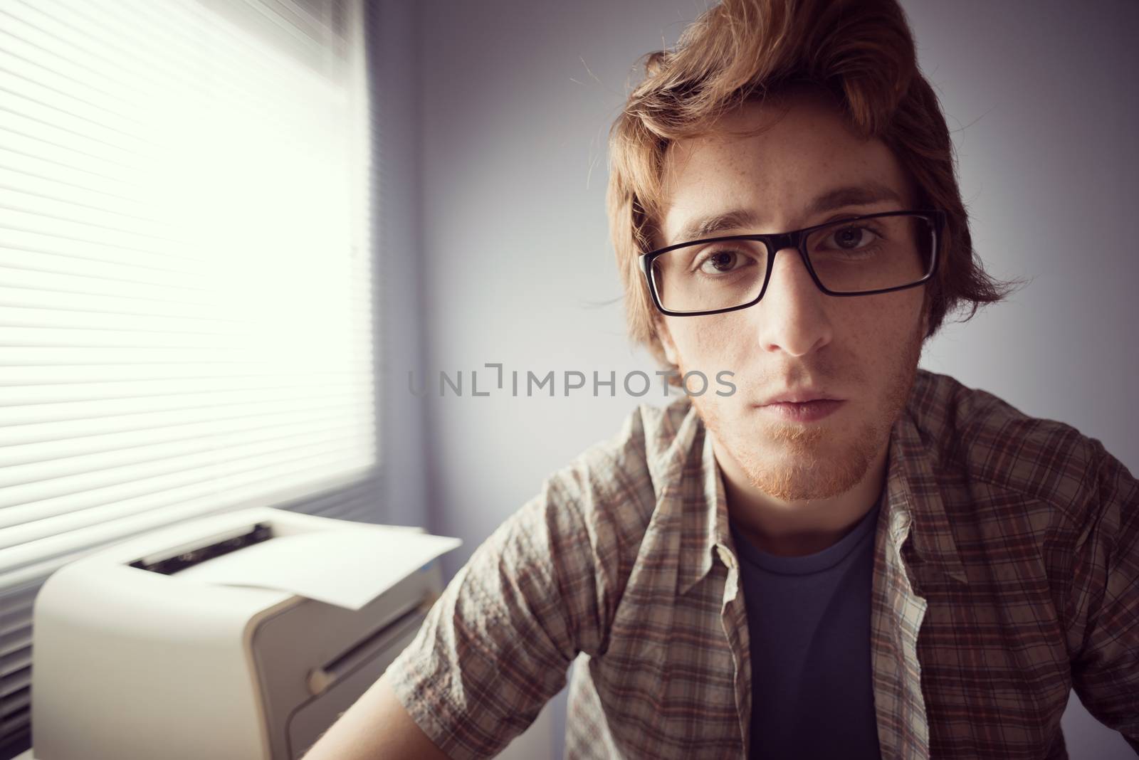 Young nerd guy staring at monitor with pensive expression.