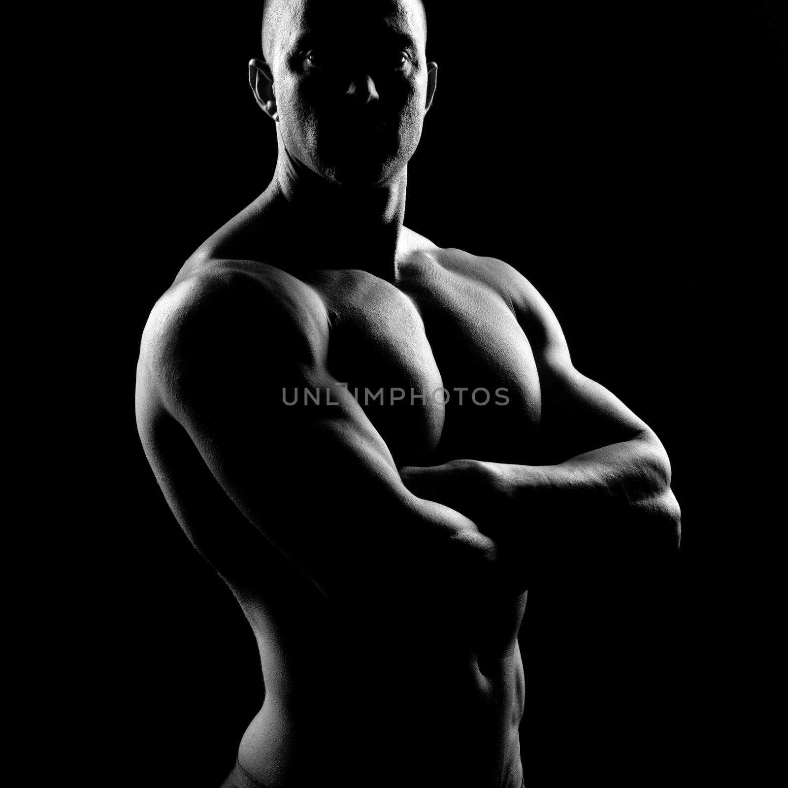 Attractive body builder posing and showing off muscles on dark background.