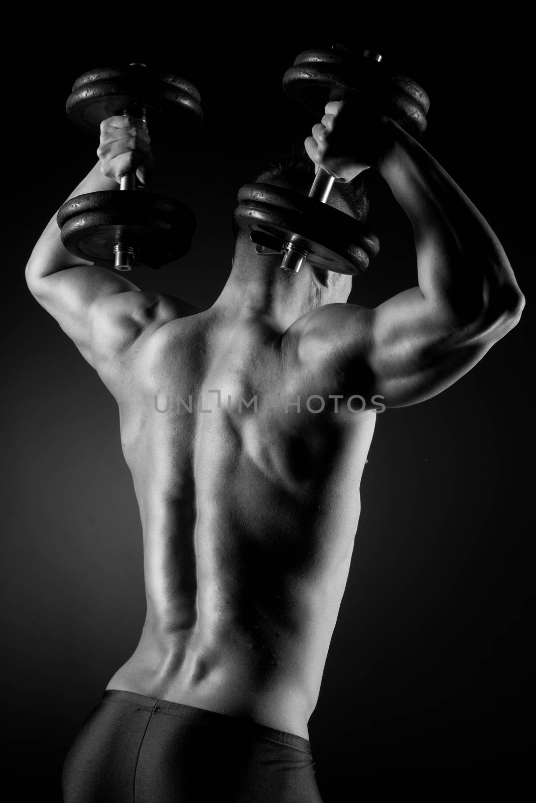 Muscular attractive man weightlifting on dark background.