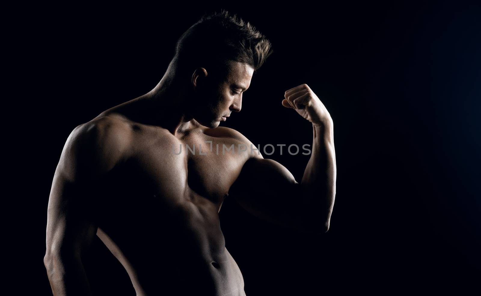 Body builder posing and showing off bicep muscle on dark background.