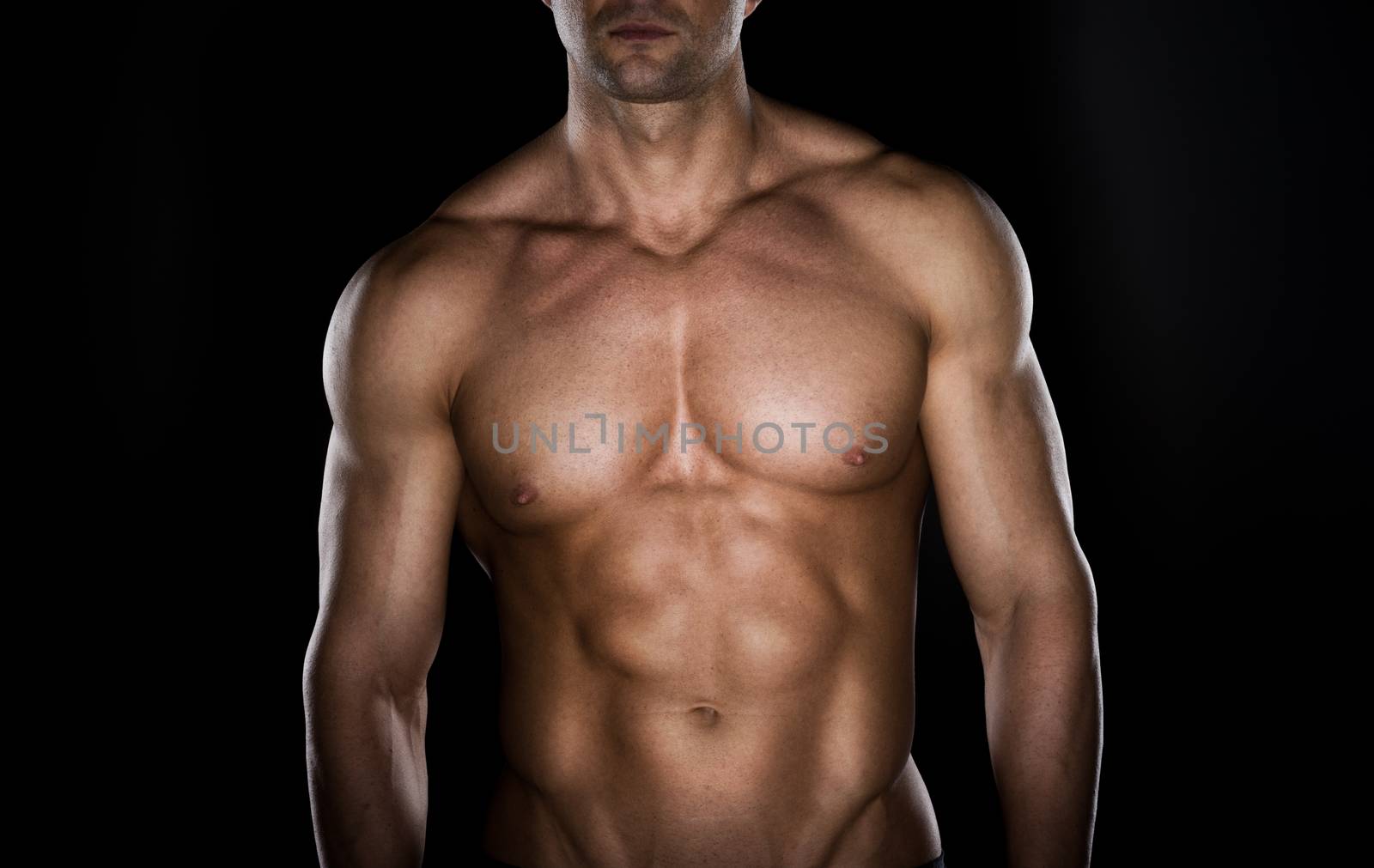 Bare chested muscular man looking down on dark background.