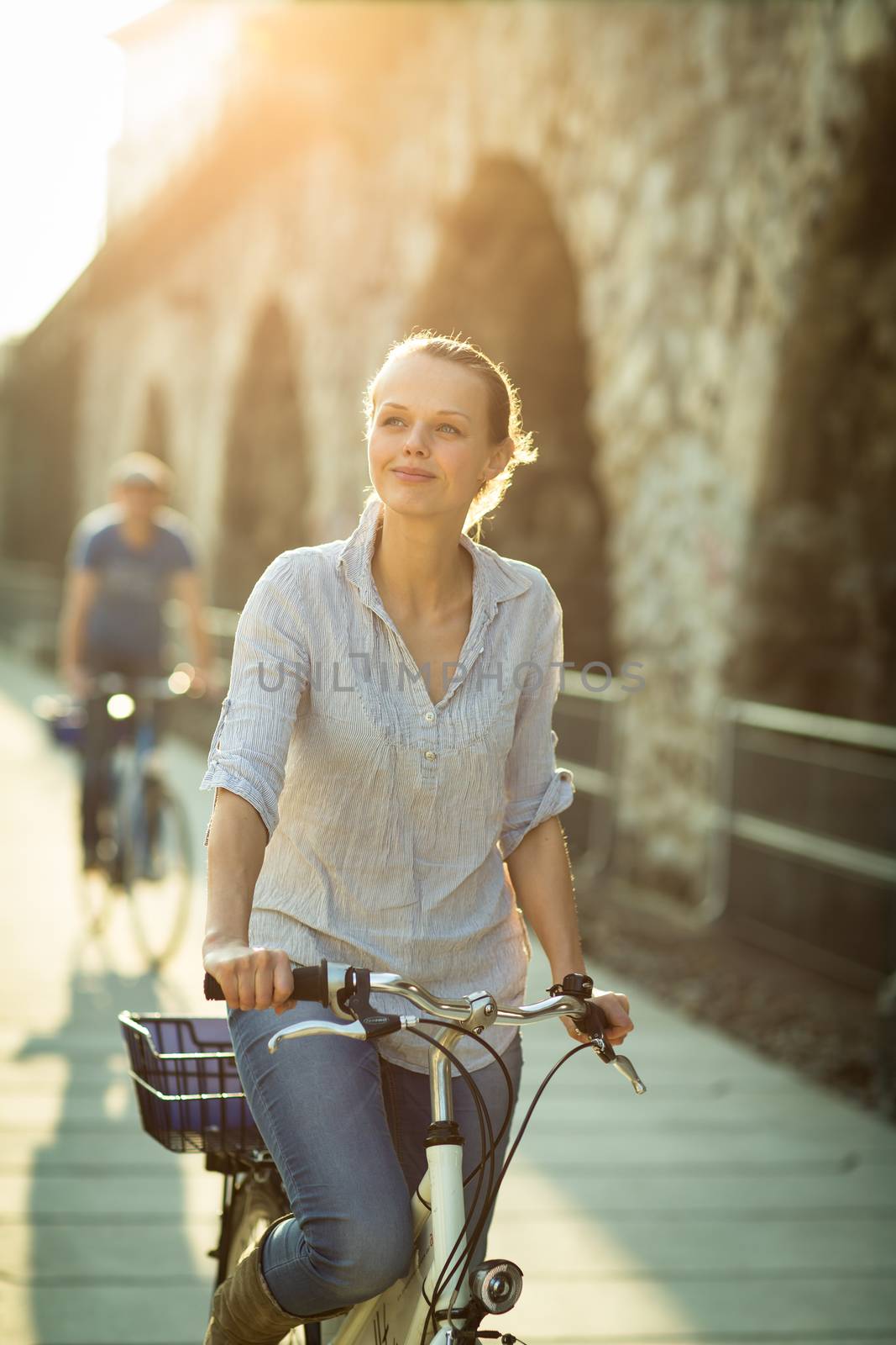 Pretty, young woman riding a bicycle in a city with her boyfriend (color toned image; shallow DOF)