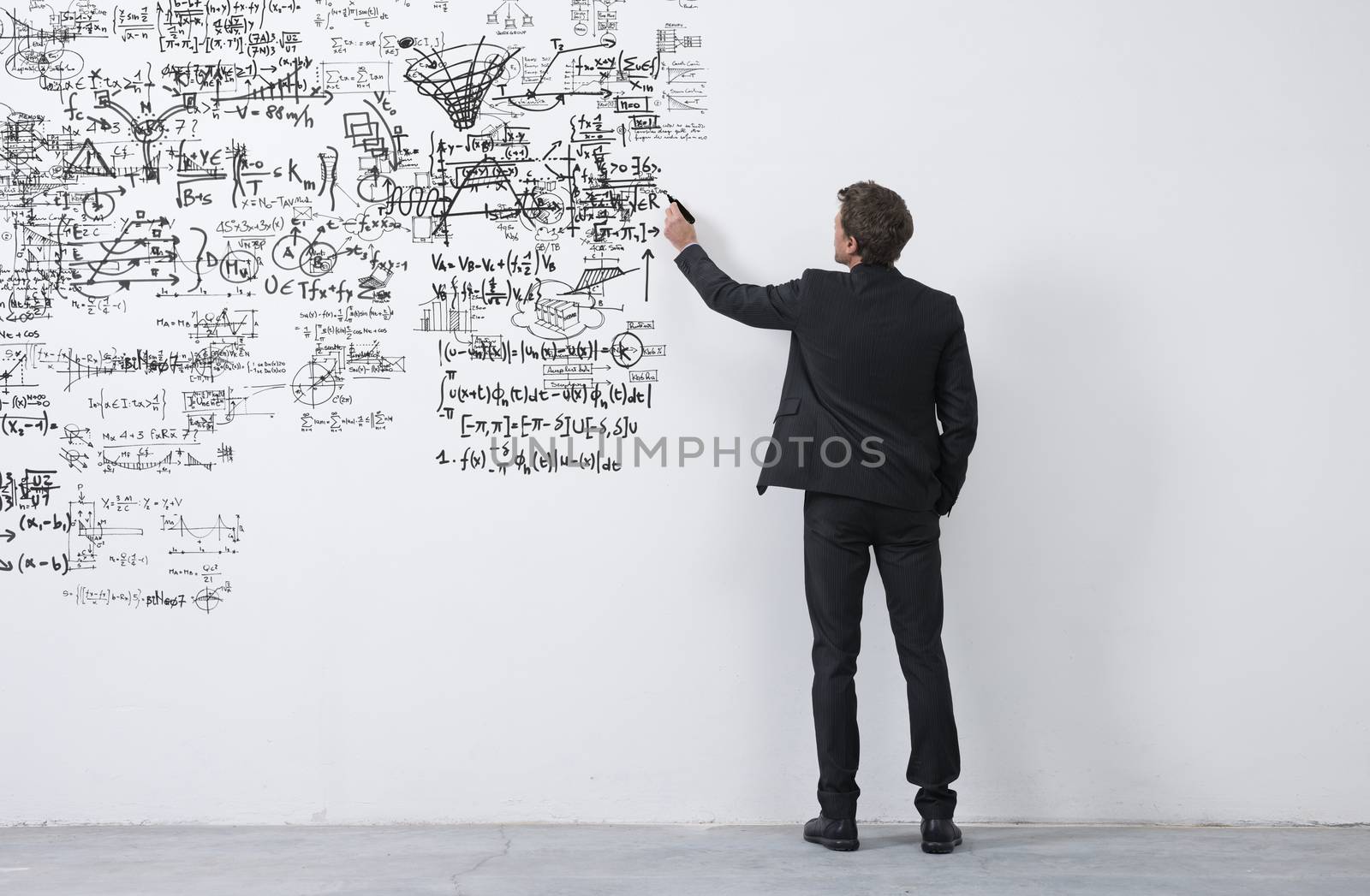 Elegant businessman rear view sketching with a black marker on a white wall.