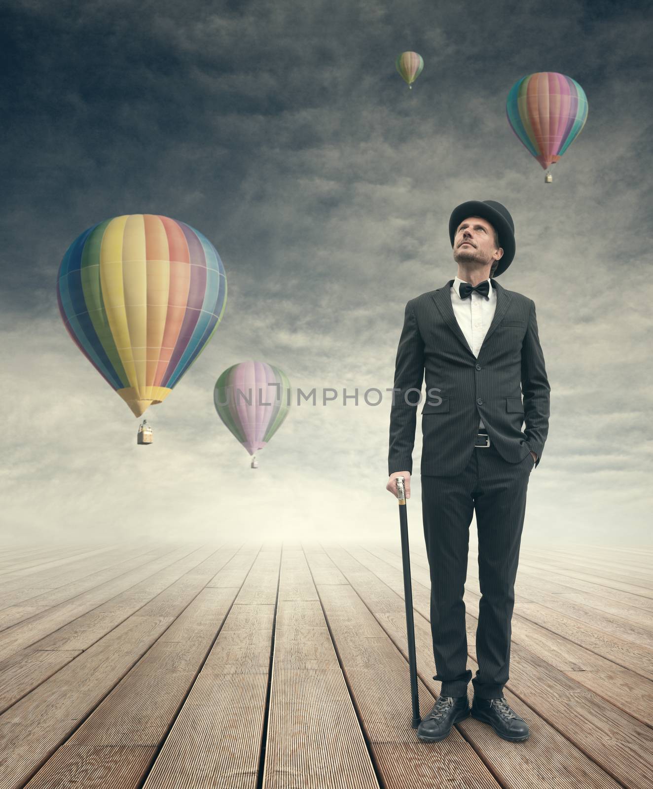 Attractive elegant businessman looking up at hot air balloons in the sky.