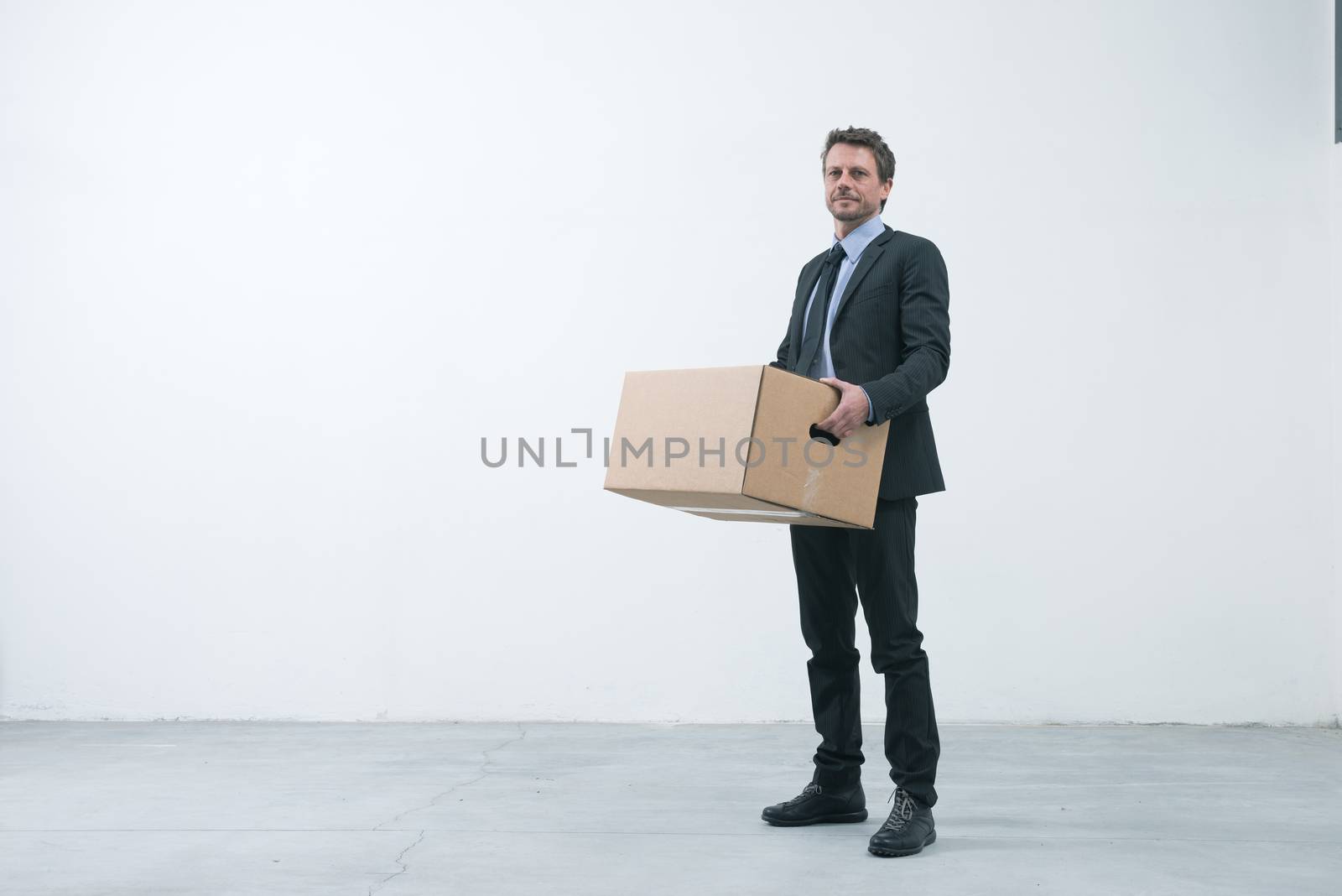 Smiling businessman holding a cardboard box and standing into an empty new office.