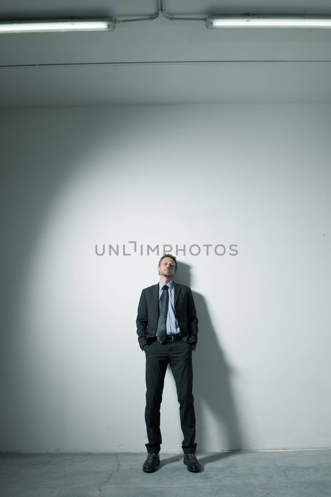 Attractive businessman leaning on a wall with hands in pockets and dramatic lighting.