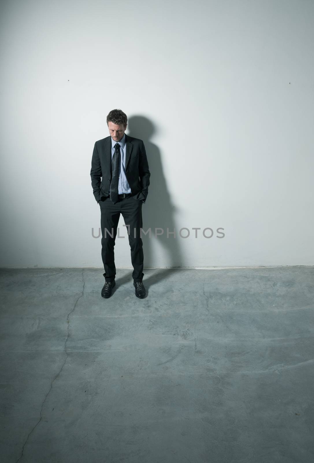 Tired pensive businessman standing with hands in pockets in an empty room with dramatic lighting.