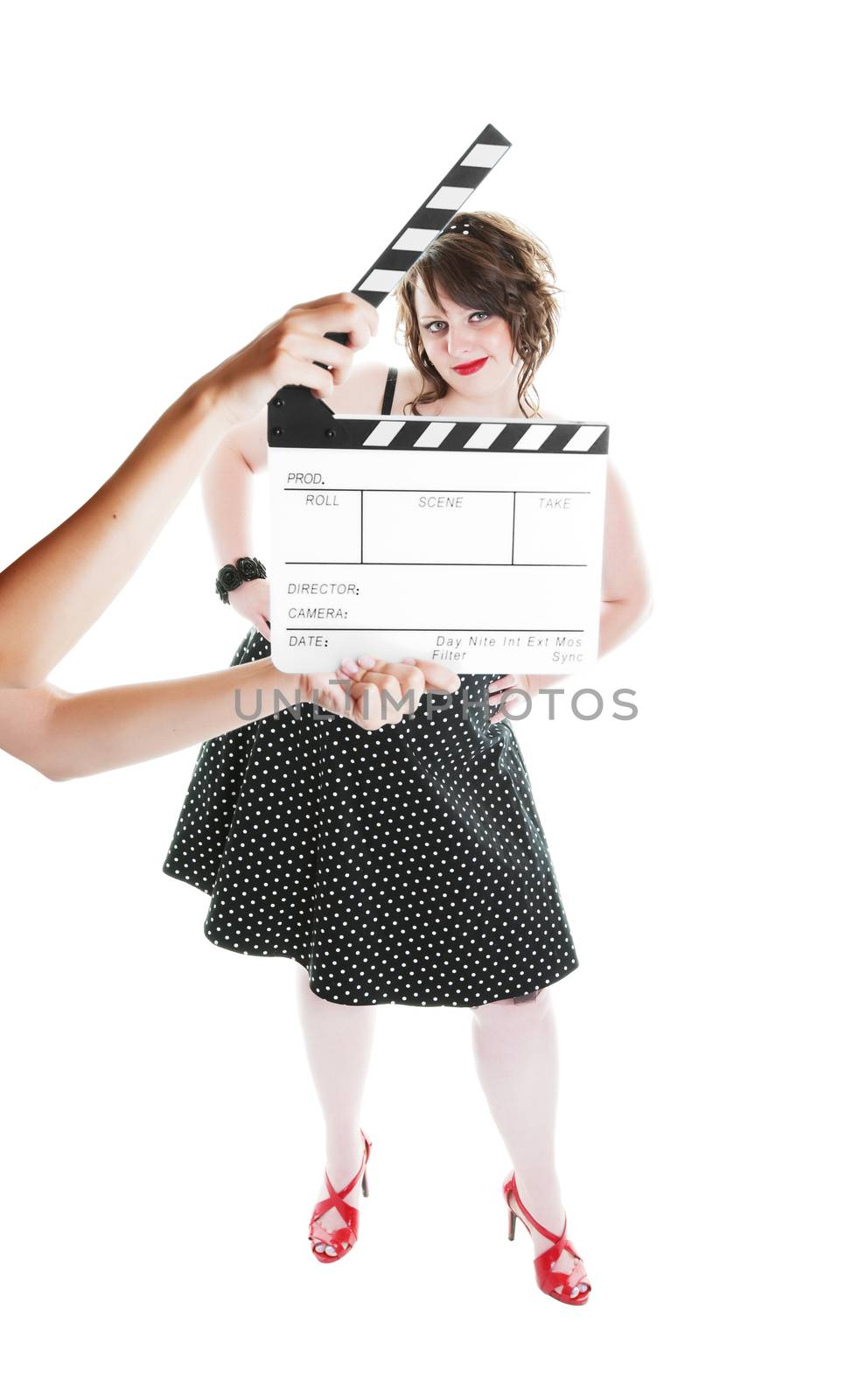 A clapper board being held up in front of a young actress dressed in pinup fashion.  Shot on white background.  Focus on actress.