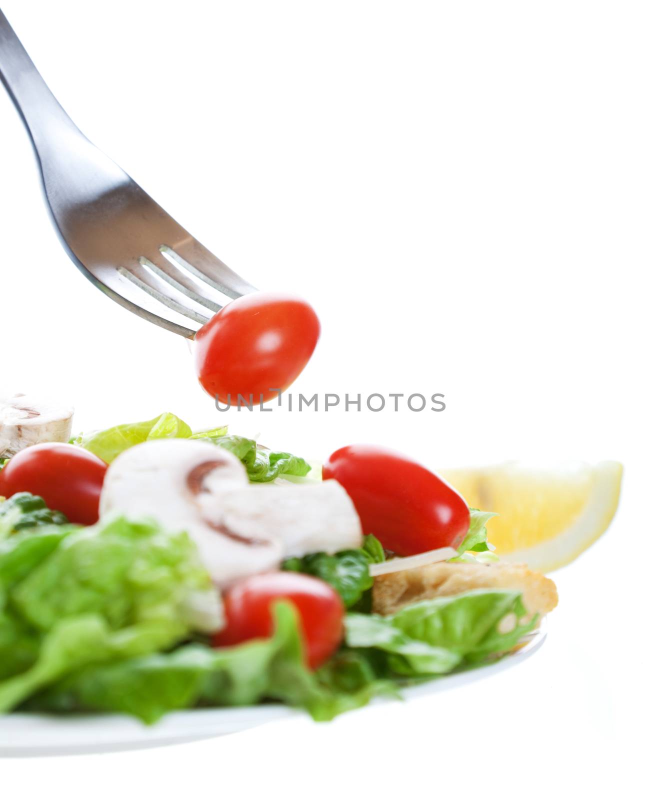A cherry tomato on a fork above a freshly tossed salad.  Shot on white background.  Shallow depth of field.