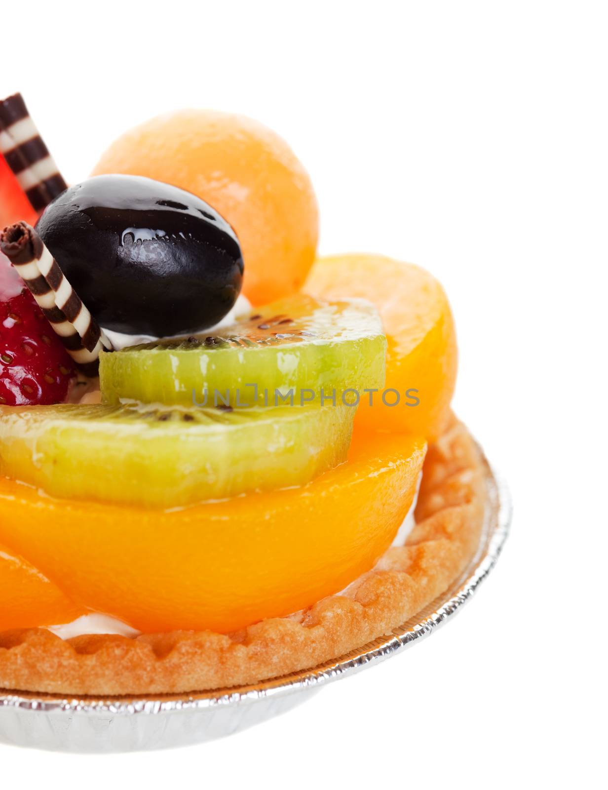 A decadent fruit tart, piled high with fresh fruit, and garnished with two delicate spikes of rolled white and milk chocolate.  Shot on white background with shallow depth of field.