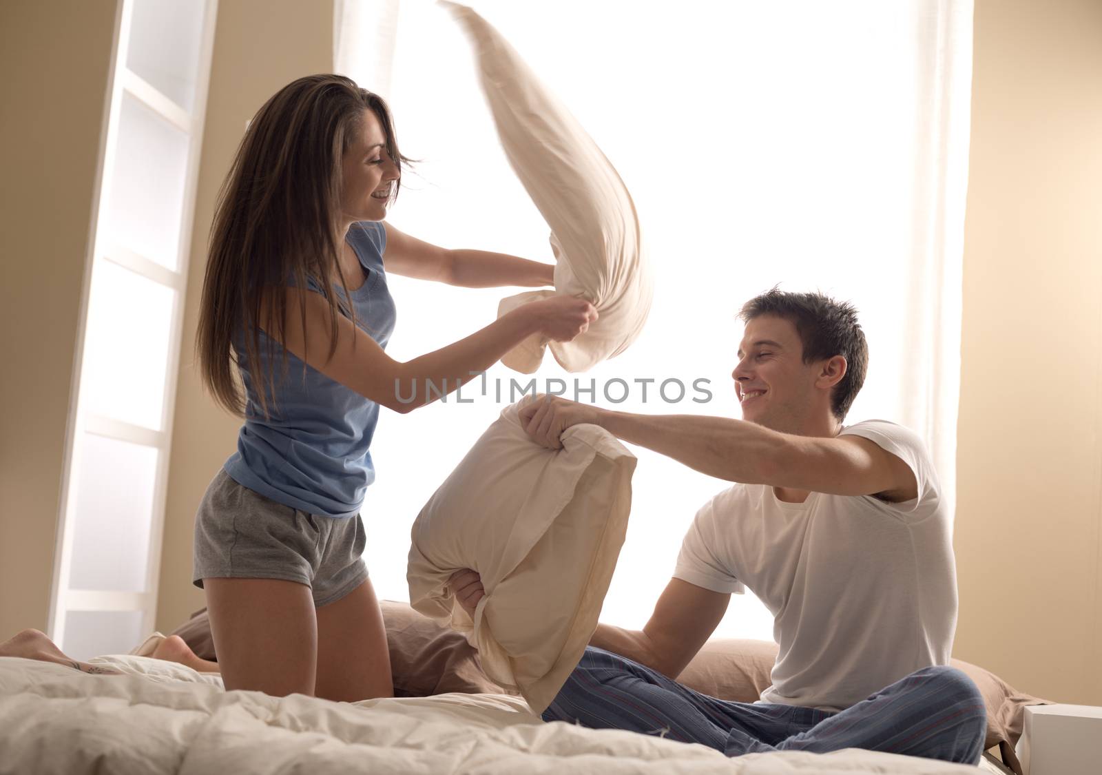 Portrait of happy loving couple having a pillow fight in bed