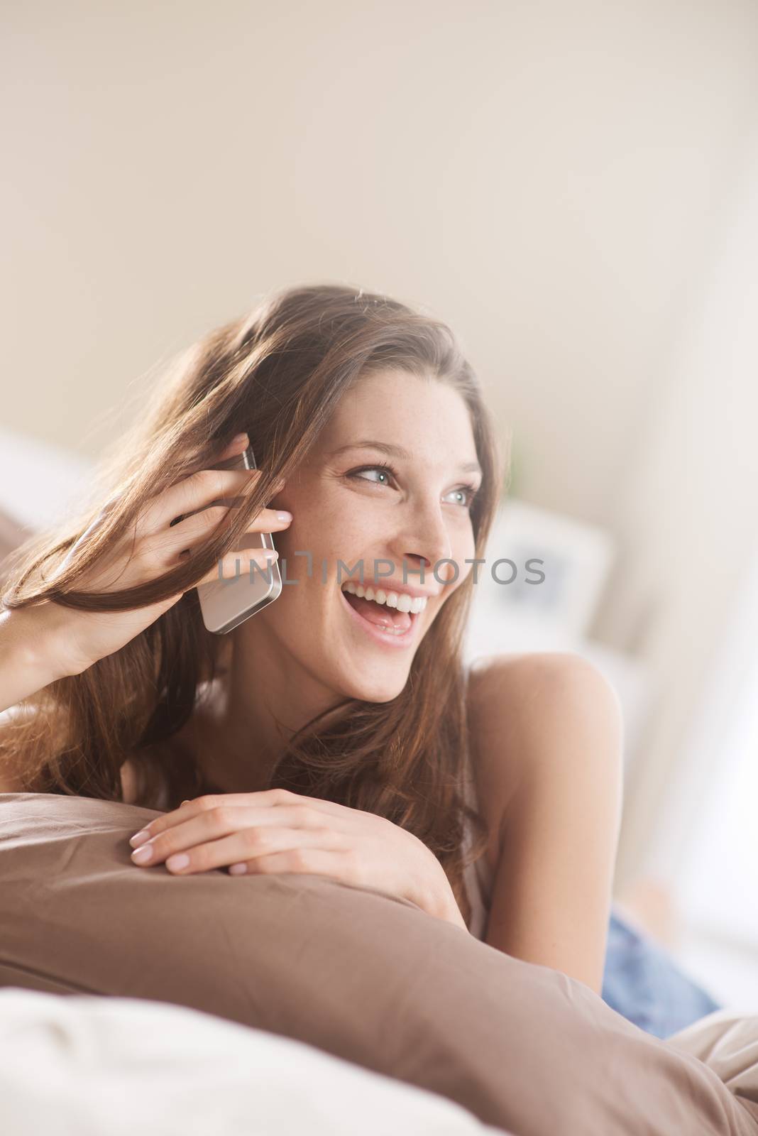 Happy young woman talking on the phone while in bed 