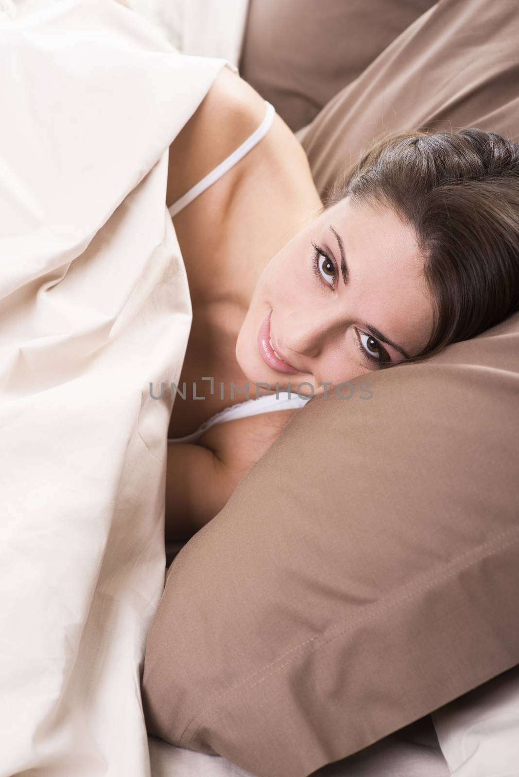 Young woman lying in bed and smiling at the camera 