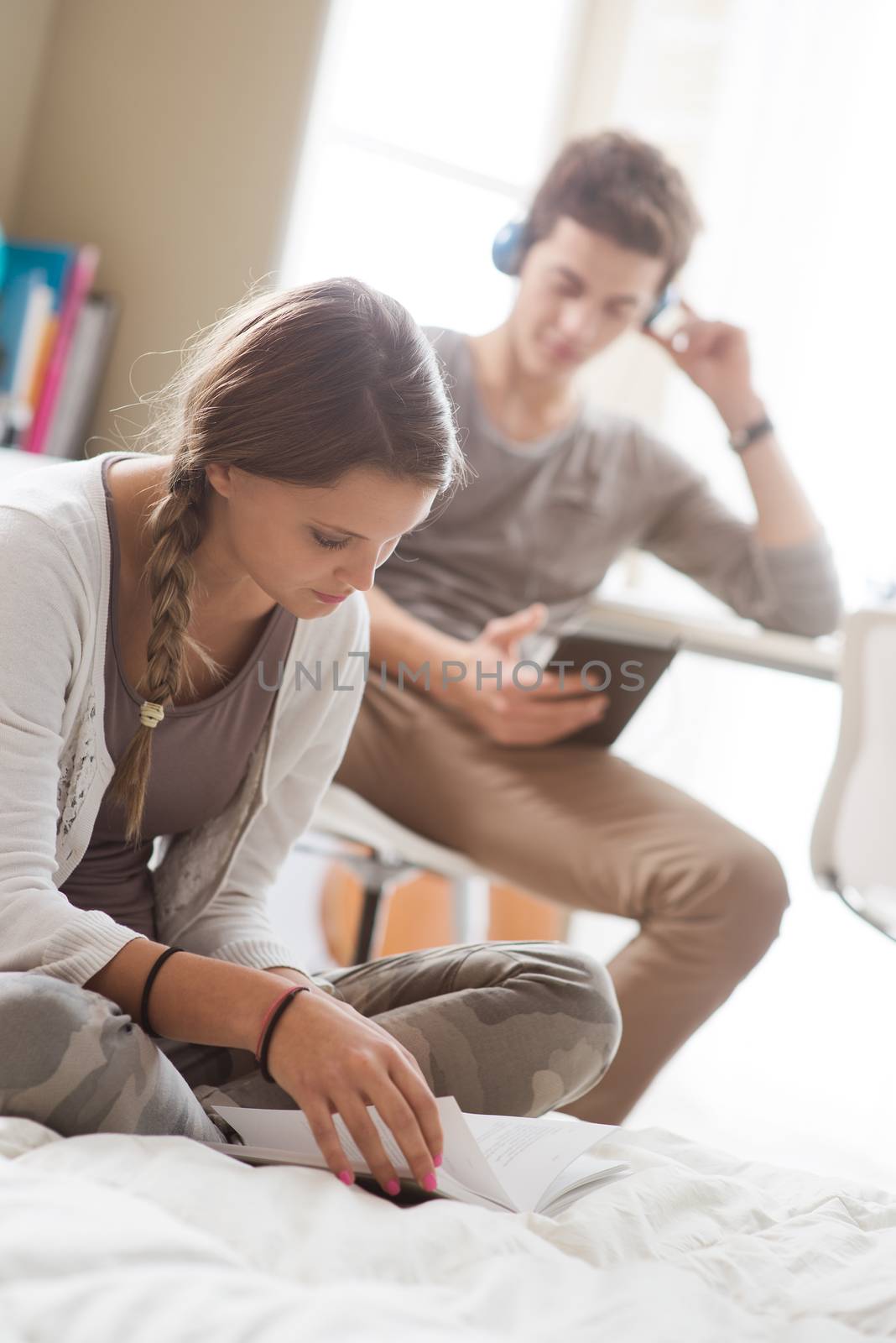 Teen boy and girl at home, sitting and studying. Girl in the foreground.
