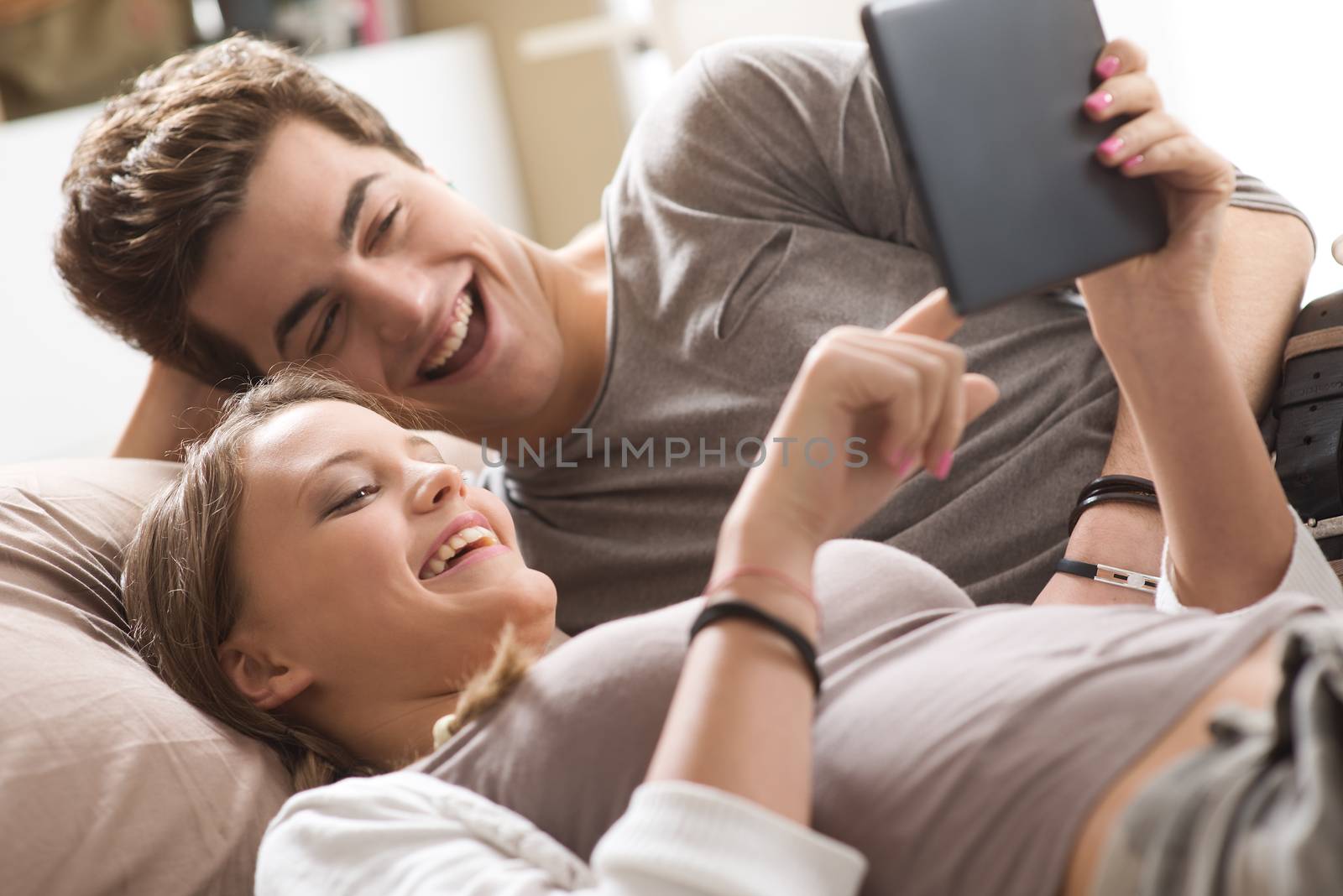 Happy young couple lying on the bed in a bedroom and using digital tablet.